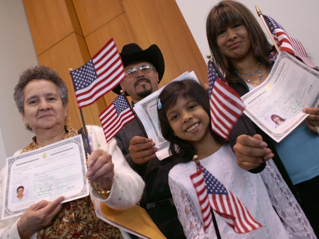 Familia hispana no identificaada en una ceremonia de naturalización en Dallas, Texas, ondean banderas de Estados Unidos.