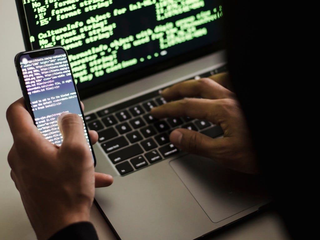 Imagen de una persona manipulando su computadora y en su celular.