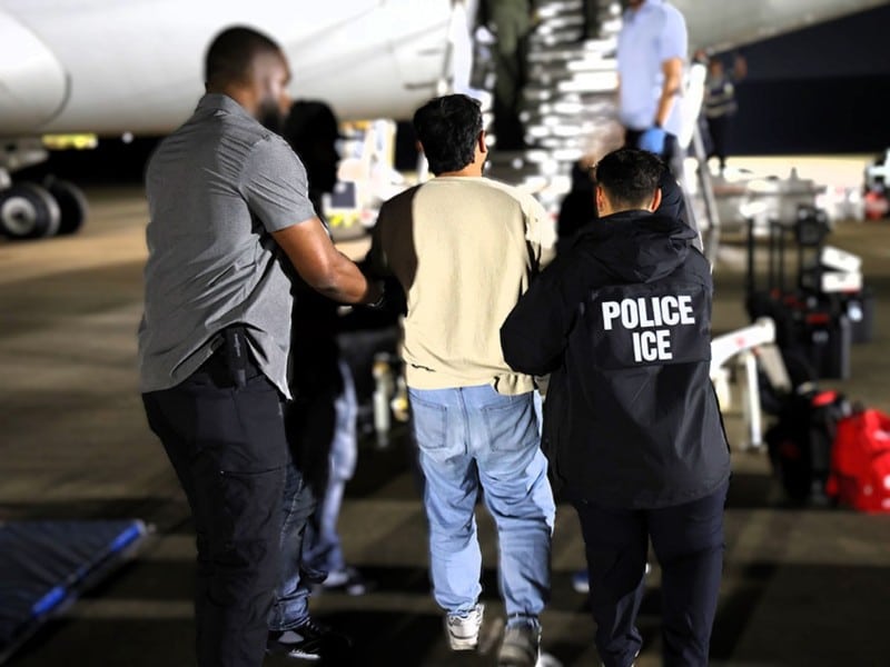 Imagen de agentes de ICE guiando a un inmigrante hacia un avión para ser deportado