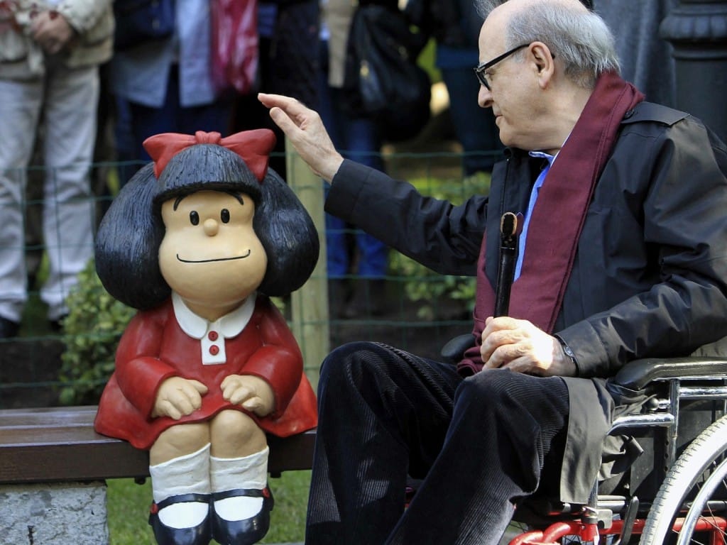 Foto de Quino junto a una escultura de su creación, Mafalda