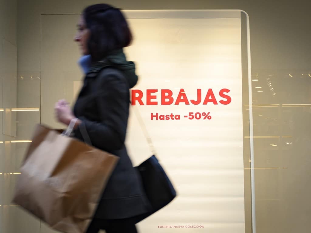 Imagen de una persona con bolsas frente a un anuncio sobre rebajas