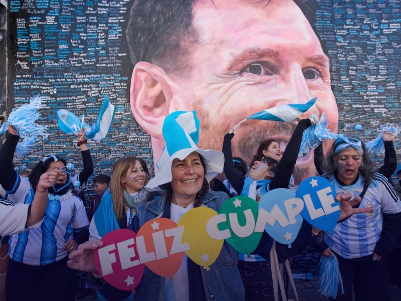 Una mujer sostiene un cartel con el mensaje de "Feliz Cumple" frente a un mural del astro argentino Lionel Messi