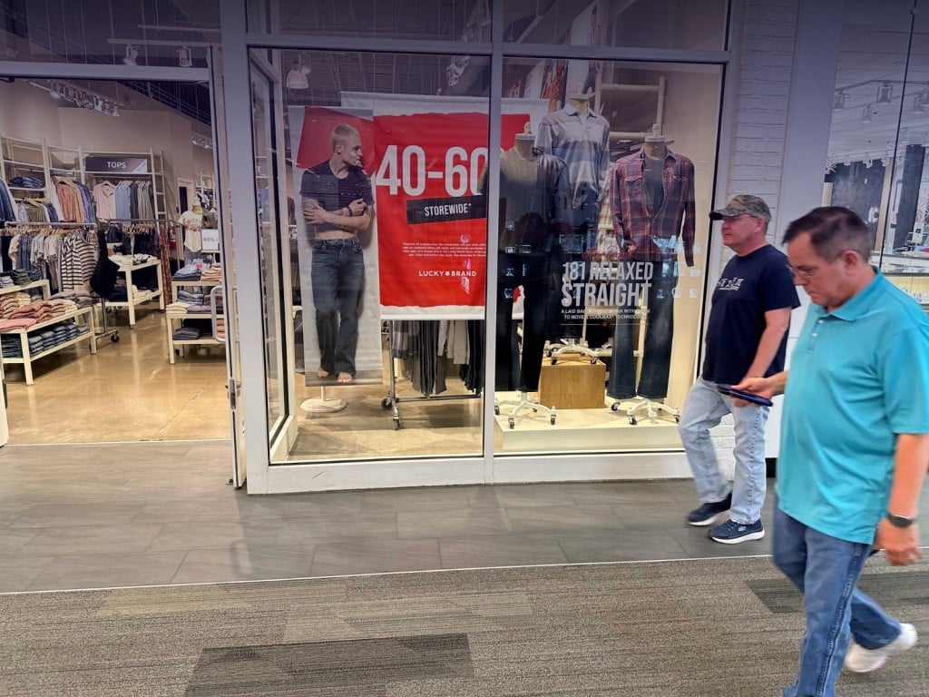 Compradores pasan frente a un letrero de descuentos en un centro comercial outlet de Lakewood, Colorado