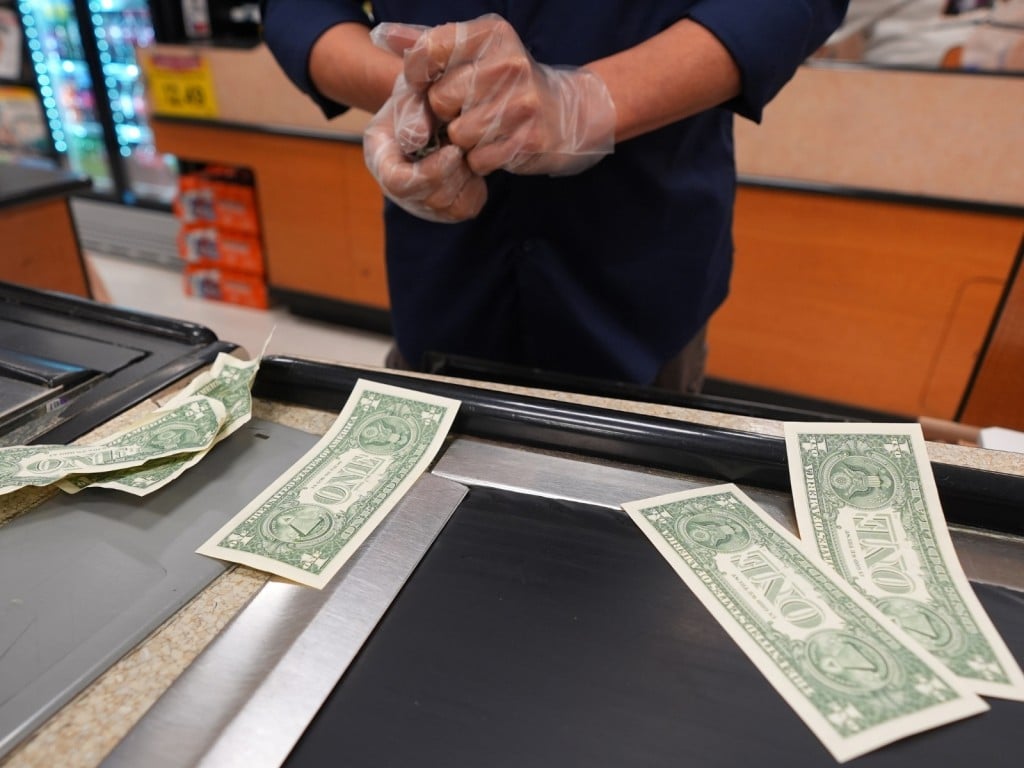Una cajera se toma una pausa mientras guarda billetes de un dólar en la caja registradora